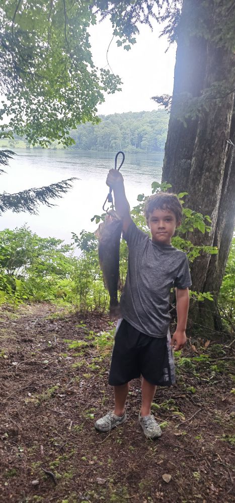 Jasper, seven years old, holding a 21-inch largemouth bass on a stringer in front of a lake, trees framing the shot.
